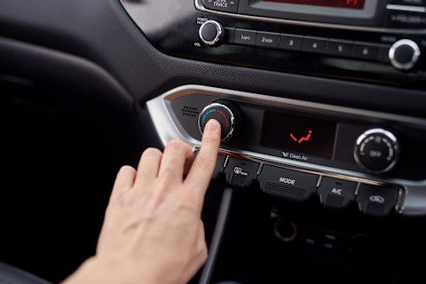 Dieses Bild zeigt eine Person, die mit dem Finger den Knopf für die Klimaanlage in ihrem Auto drückt.
