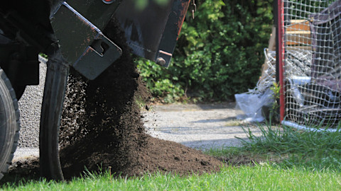 Dieses Bild zeigt, wie Mutterboden von einem LKW auf etwas Gras geschüttet wird.

