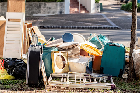 Dieses Bild zeigt eine Sammlung alter oder kaputter Gegenstände wie Koffer, Fensterläden, Schränke und andere sperrige Gegenstände am Straßenrand, die darauf warten, zur Entsorgung abgeholt zu werden.