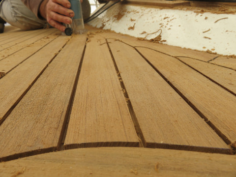 Das Bild zeigt eine Nahaufnahme von der Hand eines Handwerkers, der einen Teak-Boden abschleift.