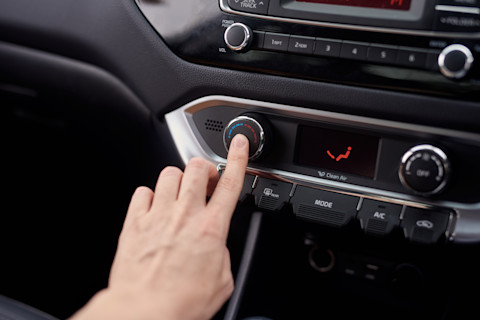 Dieses Bild zeigt eine Person, die mit dem Finger den Knopf für die Klimaanlage in ihrem Auto drückt.