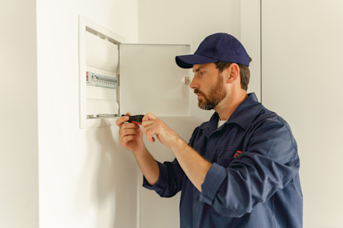Das Bild zeigt einen professionellen männlichen Elektriker, der elektrische Systeme in Häusern mit einem Schraubenzieher überprüft und repariert.
