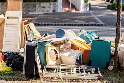 Dieses Bild zeigt eine Sammlung alter oder kaputter Gegenstände wie Koffer, Fensterläden, Schränke und andere sperrige Gegenstände am Straßenrand, die darauf warten, zur Entsorgung abgeholt zu werden.