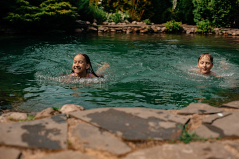 Das Bild zeigt zwei Kinder, die in einem Schwimmteich schwimmen.