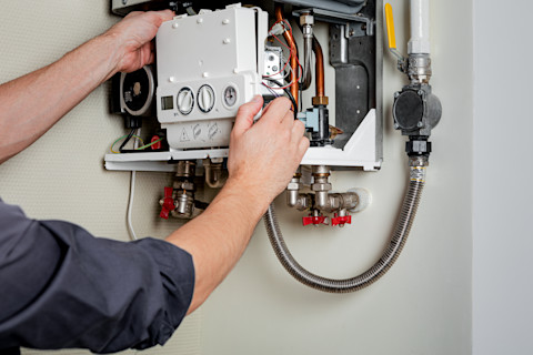 Dieses Bild zeigt einen Handwerker, der einen Gaskessel an einer weißen Wand installiert.
