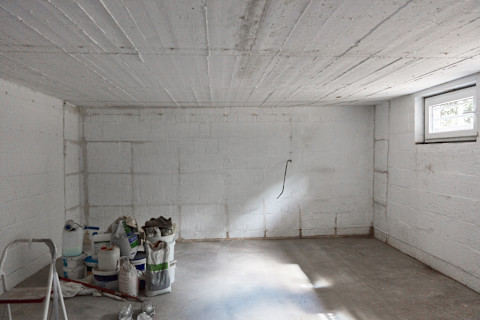 Das Bild zeigt einen Keller unter Konstruktion, mit mehreren Baumaterialien und Werkzeugen im Vordergrund.