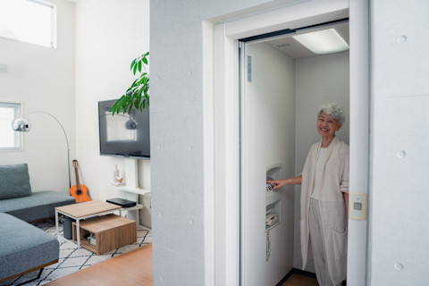 Das Bild zeigt eine Frau, die in ihrem Zuhause einen Lift benutzt, bei dem die Türe noch offensteht. Auf der linken Seite kann man das Wohnzimmer erkennen.