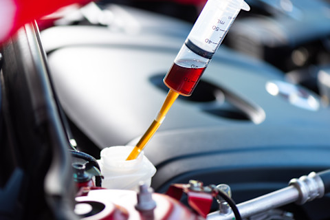 Das Bild zeigt eine Nahaufnahme eines Vorgangs, bei dem eine Flüssigkeit mit einer Spritze in einen Behälter, vermutlich in einem Fahrzeugmotor, eingefüllt wird. Es könnte sich um Motoröl oder eine andere notwendige Flüssigkeit für die Wartung des Fahrzeugs handeln. Die Spritze zeigt genaue Messungen an, um die richtige Menge der Flüssigkeit zu bestimmen. Dies ist ein üblicher Vorgang bei der Fahrzeugwartung, um die optimale Leistung und Lebensdauer des Motors zu gewährleisten.