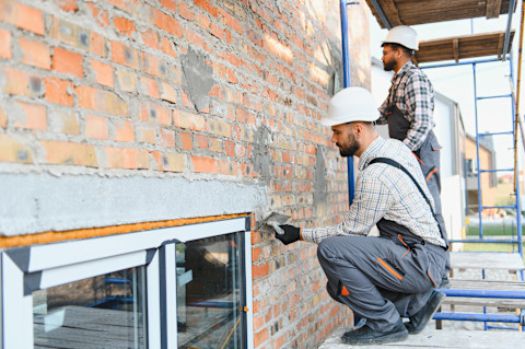 Zwei Handwerker verputzen eine Außenfassade.