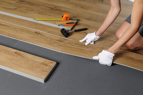 Ein Handwerker verlegt Vinylboden in einem hellen Wohnraum.