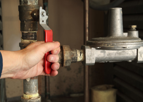 Das Bild zeigt einen Techniker mit einem Gasdruckregler vor einem Absperrventil. Es ist nur die Hand zu sehen.