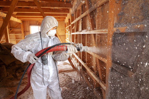 Das Bild zeigt einen Mann in Schutzkleidung und Maske, der eine Wand mit Spritzzellulose isoliert.