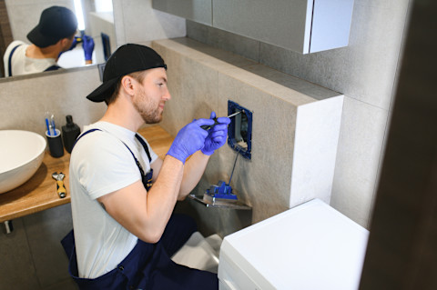 Das Bild zeigt einen Klempner, der eine Toilette installiert.