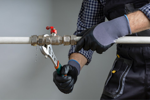 Das Bild zeigt einen Handwerker, der eine Wasserleitung repariert.