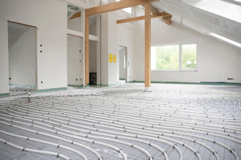 Das Bild zeigt den Einbau einer Fußbodenheizung in einem Neubau. Die Heizrohre sind in Schleifenmuster über den Boden verlegt und werden später unter einem Estrich verborgen, um eine gleichmäßige Wärmeverteilung im Raum zu gewährleisten. Diese Art der Heizung ist besonders energieeffizient und sorgt für eine behagliche Wärme. Fußbodenheizungen werden häufig in Neubauten oder bei Renovierungen installiert, um eine moderne und komfortable Heizlösung zu bieten.