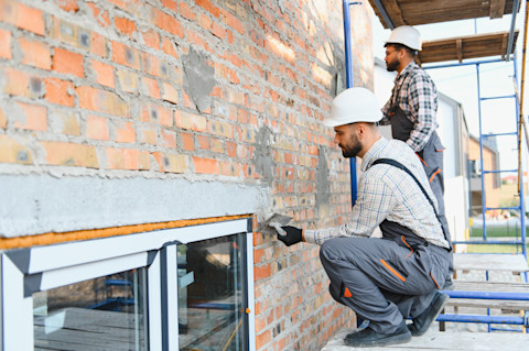 Zwei Handwerker verputzen eine Außenfassade.