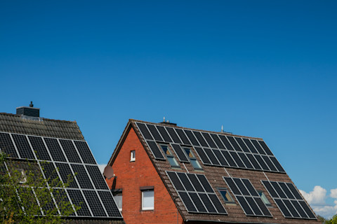 Das Bild zeigt zwei Dächer, die mit Solarzellen bedeckt sind vor einem blauen Himmel.