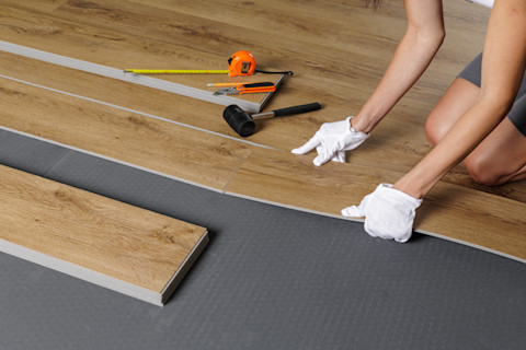 Ein Handwerker verlegt Vinylboden in einem hellen Wohnraum.