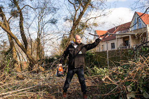 Gartenbauer sortiert nach einem Baumschnitt die abgesägten Äste im Garten.